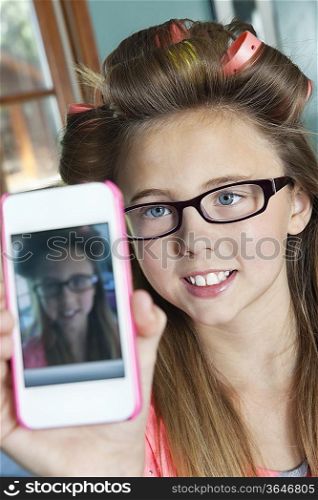 Little girl with hair curlers photographing herself with cell phone