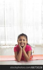 Little girl with hand on chin lying on yoga mat