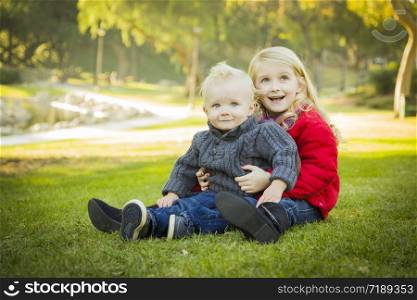 Little Girl with Her Baby Brother Wearing Winter Coats Outdoors Sitting at the Park.