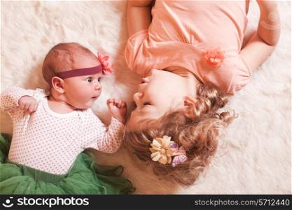 Little girl with her newborn sister on a fur carpet