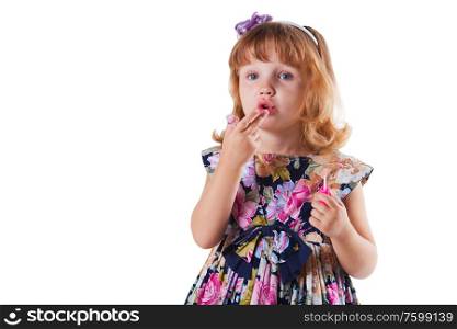 Little girl with lipstick in hand; she is touching her lips, she stands on white background