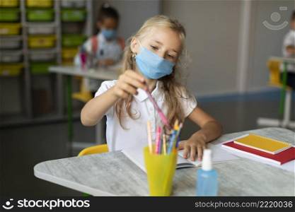 little girl with medical mask taking pencil
