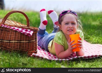 Little girl with picnic basket and plastic cup at forest