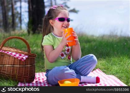 Little girl with plastic cup and picnic basket at forest