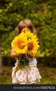 Little girl with sunflowers in the garden. Girl in the garden