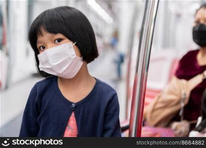 Little girl with surgical mask face protection flu and Virus outbreak in public transportation  skytrain or subway . Concept of New normal lifestyle, Using public transport to travel to school.