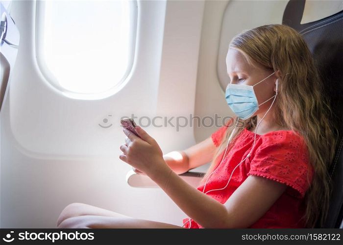 Little girl with surgical mask face protection traveling by an airplane. Protection against Coronavirus and gripp. Adorable little girl traveling by an airplane.