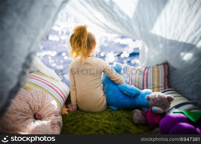 Little girl with teddy bear in camp tent looking at the sea. Little girl with teddy bear in camp tent looking at the sea.