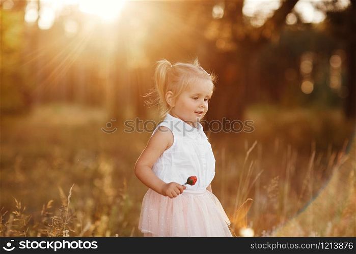 little girl with two tails. The girl walks in the park at sunset. nice little baby in a pink skirt. The girl walks in the park at sunset. nice little baby in a pink skirt