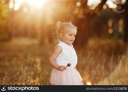 little girl with two tails. The girl walks in the park at sunset. nice little baby in a pink skirt. The girl walks in the park at sunset. nice little baby in a pink skirt