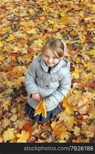 little girl with yellow leaves standing in the park