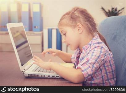 Little girl working on the laptop at home, sweet schoolgirl doing homework using wireless internet, typing on the computer, back to school concept