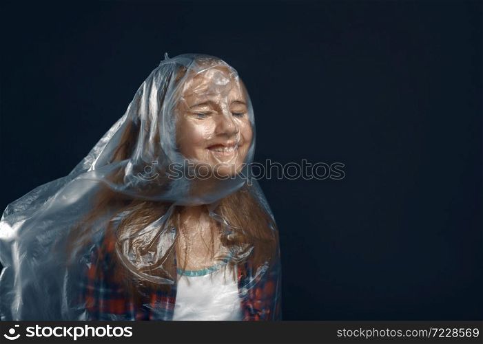 Little girl wrapped in film standing against powerful airflow in studio, developing hairstyle effect. Children and wind, kid isolated on dark background, child emotion. Child wrapped in film against powerful airflow