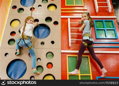 Little girlfriends on climbing wall in the entertainment center. Female children leisures on holidays, childhood happiness, happy kids on playground. Girlfriends on climbing wall, entertainment center