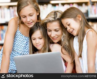 Little girls and mother with a laptop in library. Technology and fun in the library