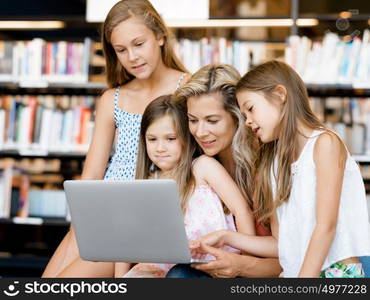 Little girls and mother with a laptop in library. Technology and fun in the library