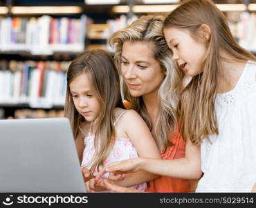 Little girls and mother with a laptop in library. Technology and fun in the library