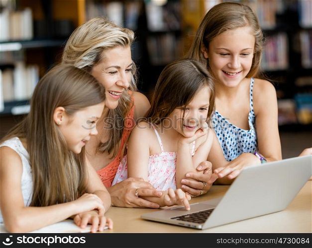 Little girls and their mum with a laptop in library. Technology and fun in the library