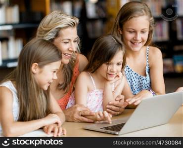 Little girls and their mum with a laptop in library. Technology and fun in the library