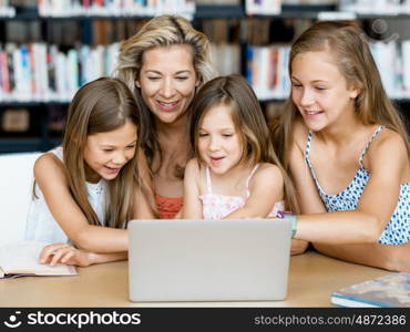 Little girls and their mum with a laptop in library. Technology and fun in the library