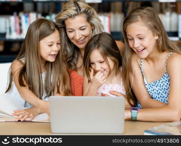 Little girls and their mum with a laptop in library. Technology and fun in the library