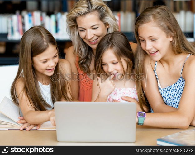 Little girls and their mum with a laptop in library. Technology and fun in the library