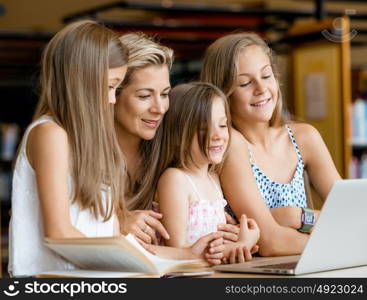 Little girls and their mum with a laptop in library. Technology and fun in the library