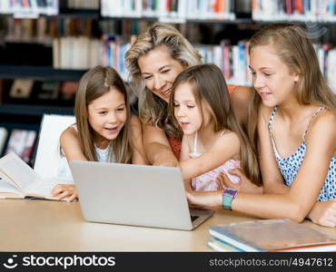 Little girls and their mum with a laptop in library. Technology and fun in the library