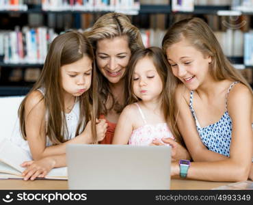 Little girls and their mum with a laptop in library. Technology and fun in the library