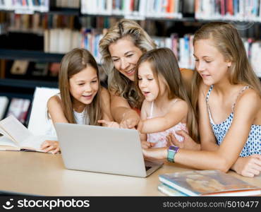 Little girls and their mum with a laptop in library. Technology and fun in the library