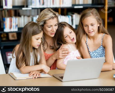 Little girls and their mum with a laptop in library. Technology and fun in the library