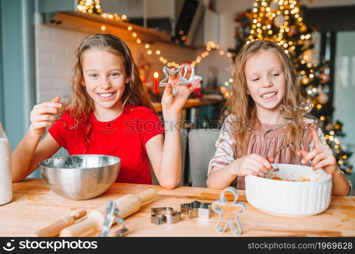 Little girls cooking Christmas gingerbread. Baking and cooking with children for Christmas at home.. Little girls making Christmas gingerbread house at fireplace in decorated living room.