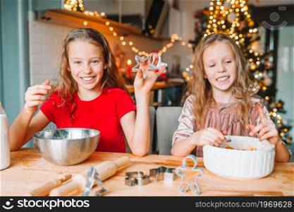 Little girls cooking Christmas gingerbread. Baking and cooking with children for Christmas at home.. Little girls making Christmas gingerbread house at fireplace in decorated living room.