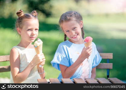 Little girls eating ice-cream outdoors at summer in outdoor cafe. Cute kids enjoying real italian gelato. Little girls eating ice-cream outdoors at summer in outdoor cafe