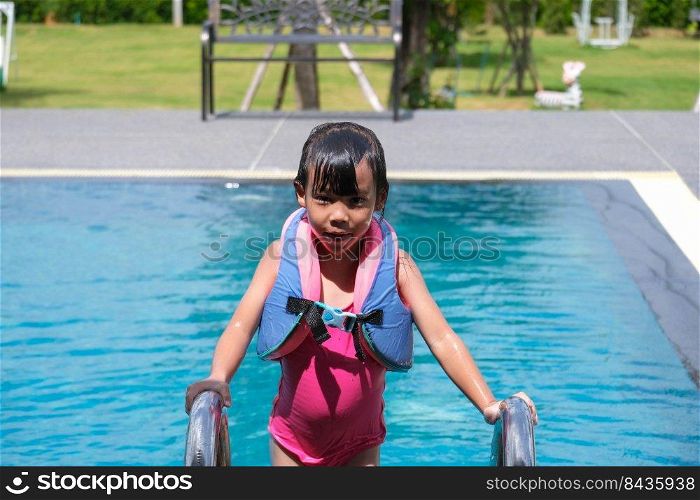 Little girls enjoy swimming in the pool. Cute Asian girl wearing a life jacket is having fun playing in the outdoor pool. Healthy Summer Activities for Kids.