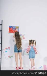 little girls hanging drawings white wall