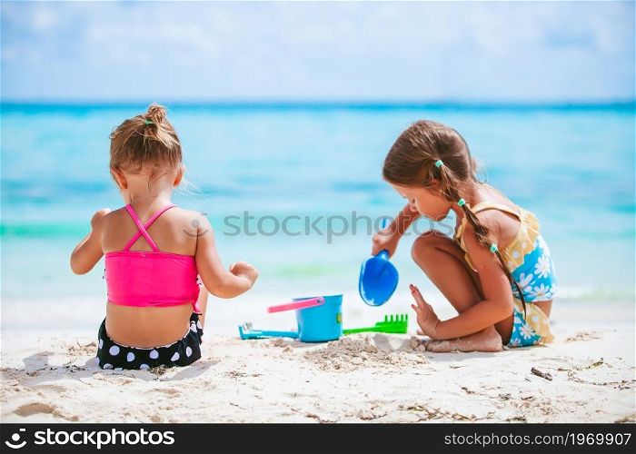 Little girls having fun at tropical beach playing together and making sandcastle. Two little happy girls have a lot of fun at tropical beach playing together