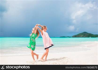 Little girls having fun at tropical beach playing together at shallow water. Adorable little sisters at beach during summer vacation. Little happy funny girls have a lot of fun at tropical beach playing together. Sunny day with rain in the sea
