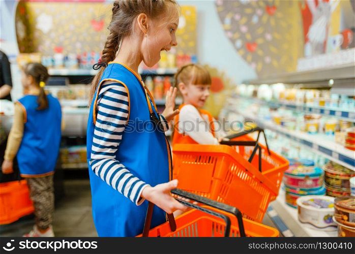 Little girls in uniform with baskets at the showcase, playroom. Kids plays sellers in imaginary supermarket, salesman profession learning, children on playground