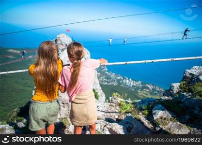 Little girls on suspension bridge in mountains. Girls crossing the chasm on the rope bridge.