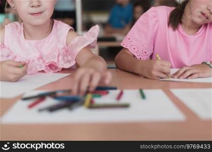 Little girls sitting in elementary school drawing on paper with their friends while sitting in a modern classroom. High quality photo. Little girls sitting in elementary school drawing on paper with their friends while sitting in a modern classroom