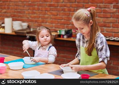 Little girls stirring the yolk with sugar. Kids taking part in baking workshop. Baking classes for children, aspiring little chefs. Girls learning to cook. Combining and stirring prepared ingredients. Real people, authentic situations