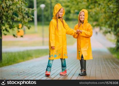 Little girls wearing waterproof coat outdoors by rainy and sunny day spring day. Adorable little girls under the rain on warm spring day