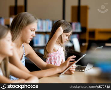 Little girls with a laptop in library. Technology and fun in the library