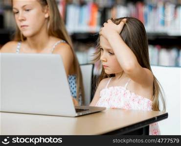 Little girls with a laptop in library. Technology and fun in the library