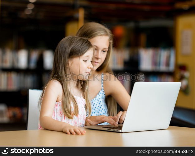 Little girls with a laptop in library. Technology and fun in the library