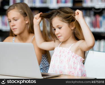 Little girls with a laptop in library. Technology and fun in the library