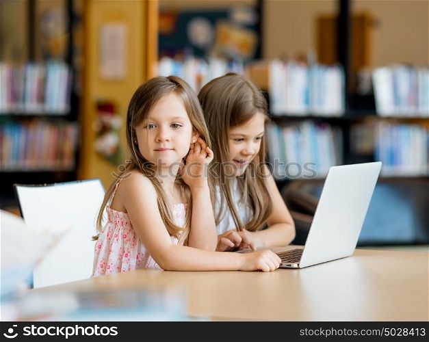 Little girls with a laptop in library. Technology and fun in the library