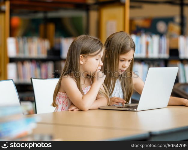 Little girls with a laptop in library. Technology and fun in the library