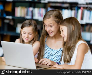 Little girls with a laptop in library. Technology in the library